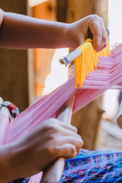 Woman in typical Guatemalan dress weaving with colored threads in the weaver - indigenous artisan woman from Guatemala making local weaving in a rural area